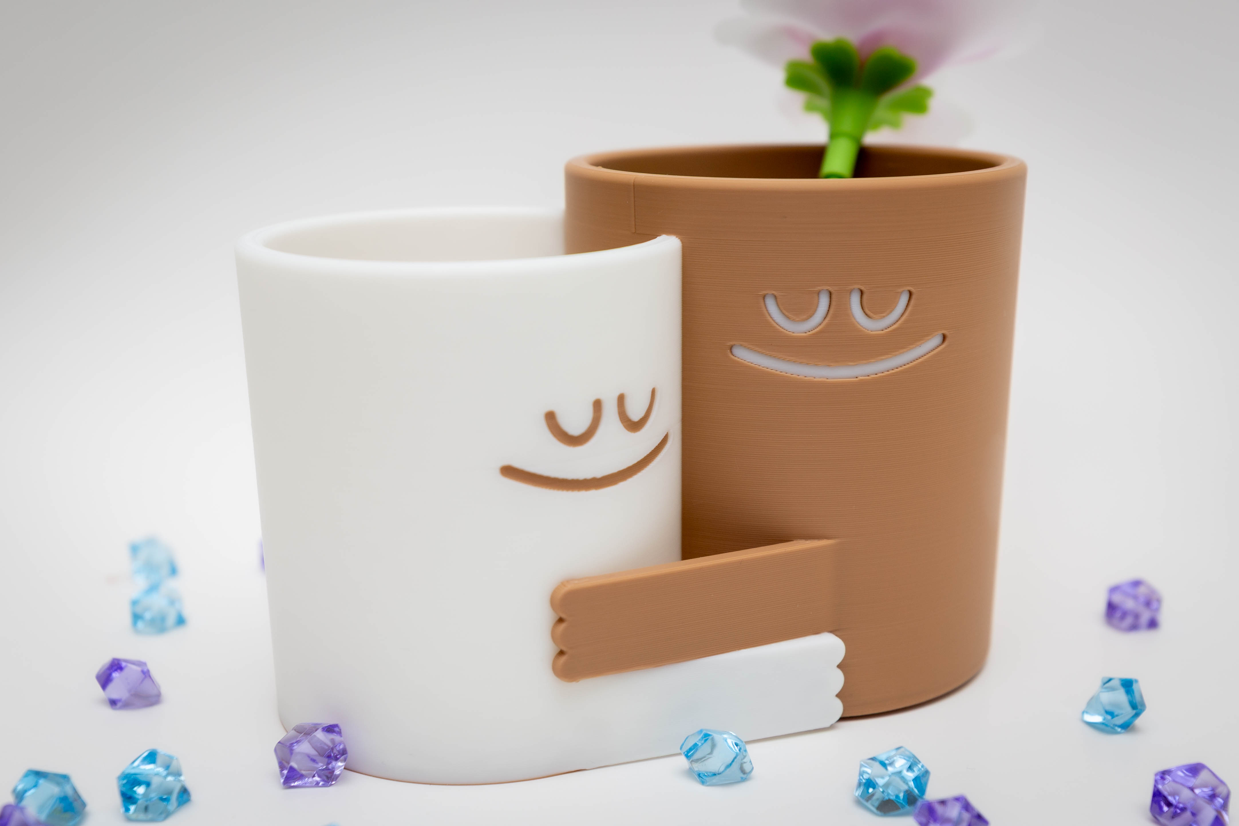 Two hugging 3D printed planters with faces on a workshop shelf